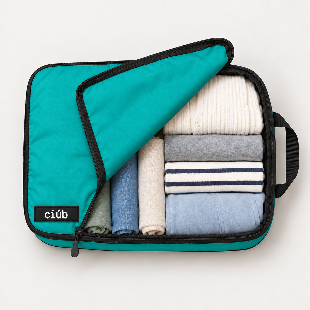 Green ciúb extra-large compression packing cube unzipped to show folded jumpers, shirts and t-shirts packed inside for travel