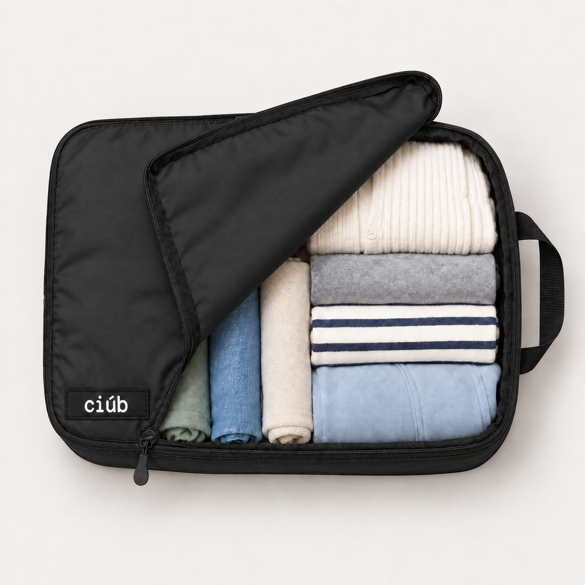 Black ciúb extra-large compression packing cube unzipped to show folded jumpers, shirts and t-shirts packed inside for travel