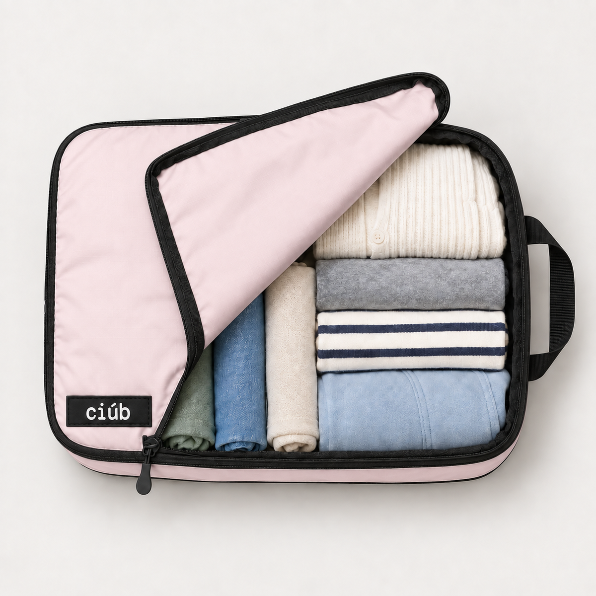 Pink ciúb extra-large compression packing cube unzipped to show folded jumpers, shirts and t-shirts packed inside for travel