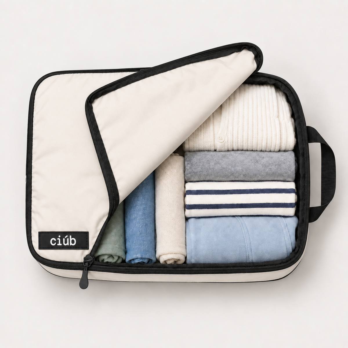 Beige ciúb extra-large compression packing cube unzipped to show folded jumpers, shirts and t-shirts packed inside for travel